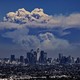 A huge cloud of smoke rises above mountains, seen in the distance behind the Los Angeles skyline.