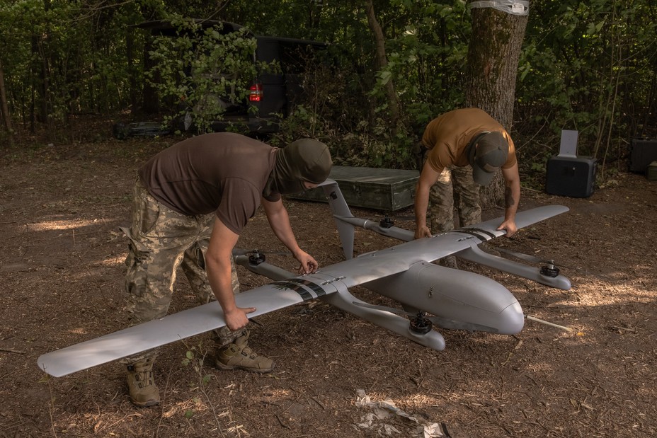 Two Ukranian soldiers bend down and position a drone on the ground.