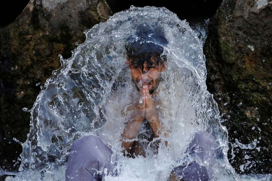 A person sits beneath a large water pipe as water splashes over their head.