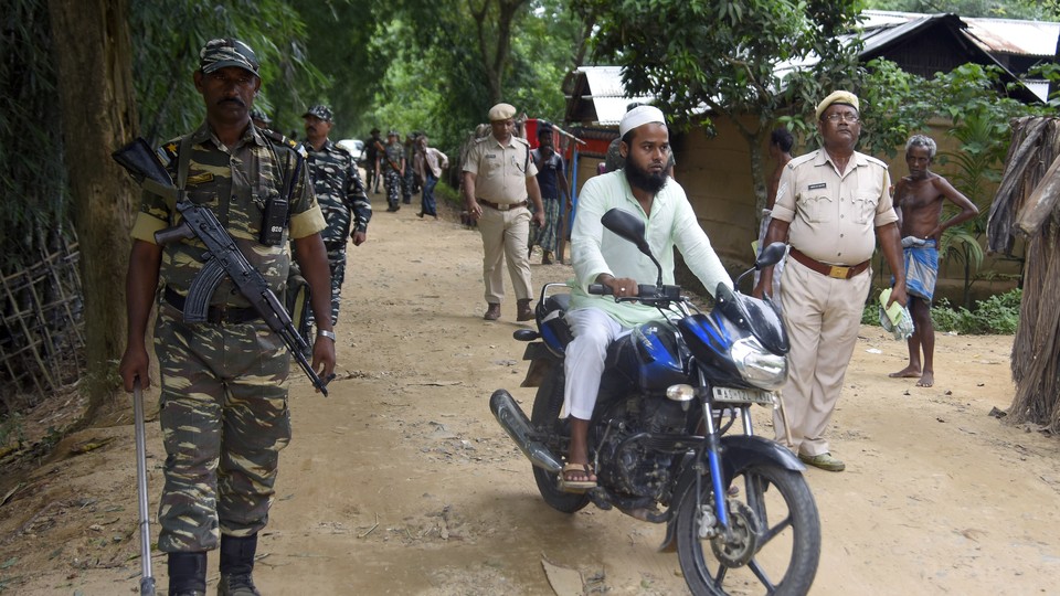 Indian security officers patrol a dirt road as a man rides past them on a motorcycle.