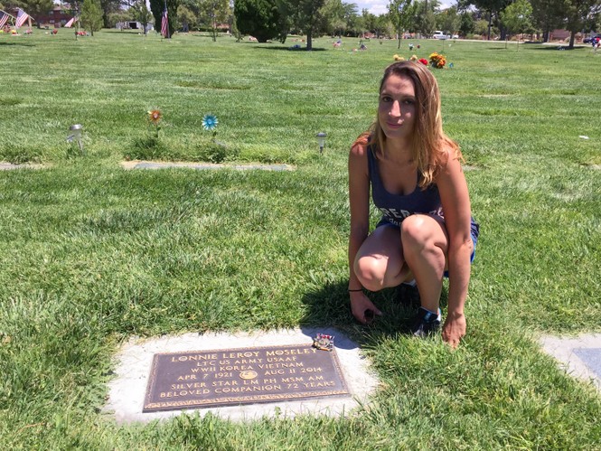 A woman kneels in the grass beside a gravestone that reads "Lonnie Leroy Moseley"