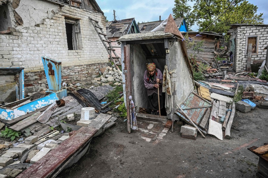 A woman stands in a cellar doorway in a heavily damaged yard.