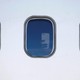 Two windows on the side of an airplane show hands holding up smartphones inside.