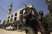 Two men with guns walk down a street in Syria.