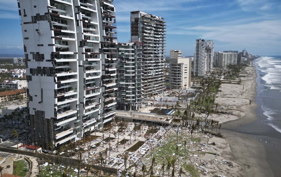 An aerial view of a long row of tall resort hotels along a beach, all heavily damaged by a storm