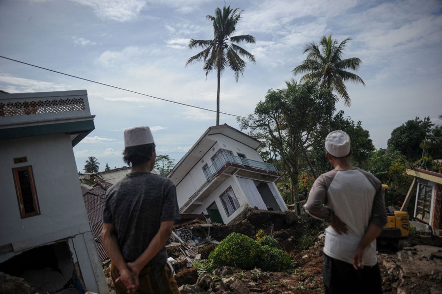Two people look at houses that have been toppled and tossed by an earthquake.