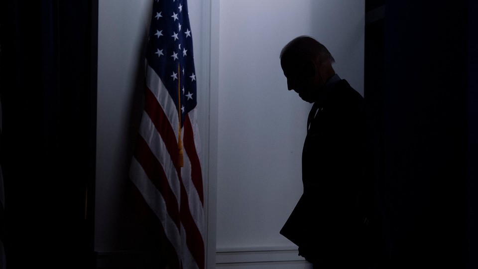 A dark photo of the silhouette of Joe Biden standing by an American flag