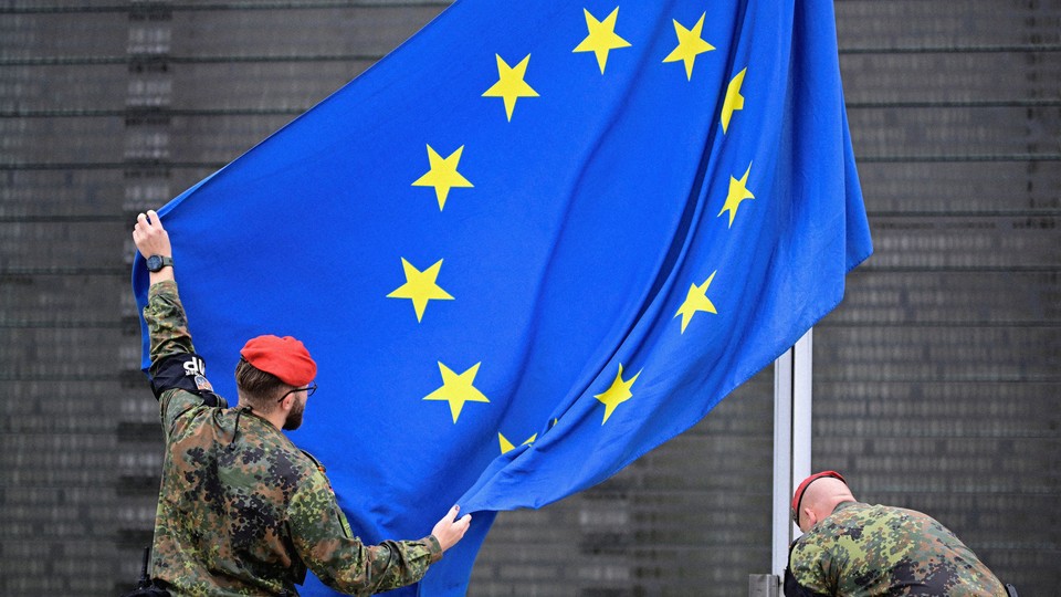 A photograph of two soldiers in red berets raising an EU flag