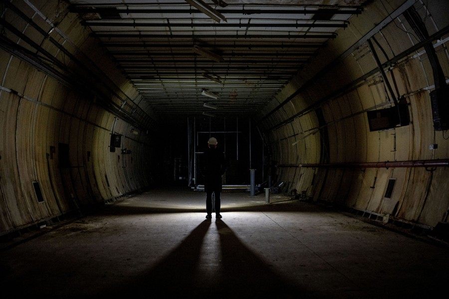 A person wearing a hardhat stands in the middle of a long, empty, dark tunnel.