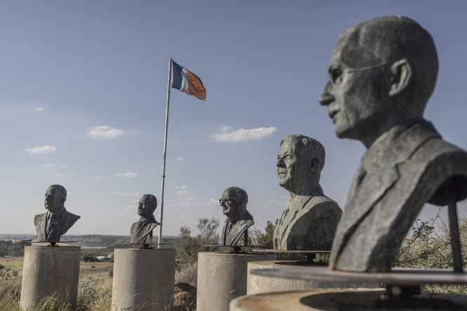 A color photograph showing bronze busts of Apartheid leaders in a field under a blue sky