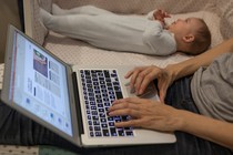 Photo showing a person working on a laptop, sitting on the floor next to a baby