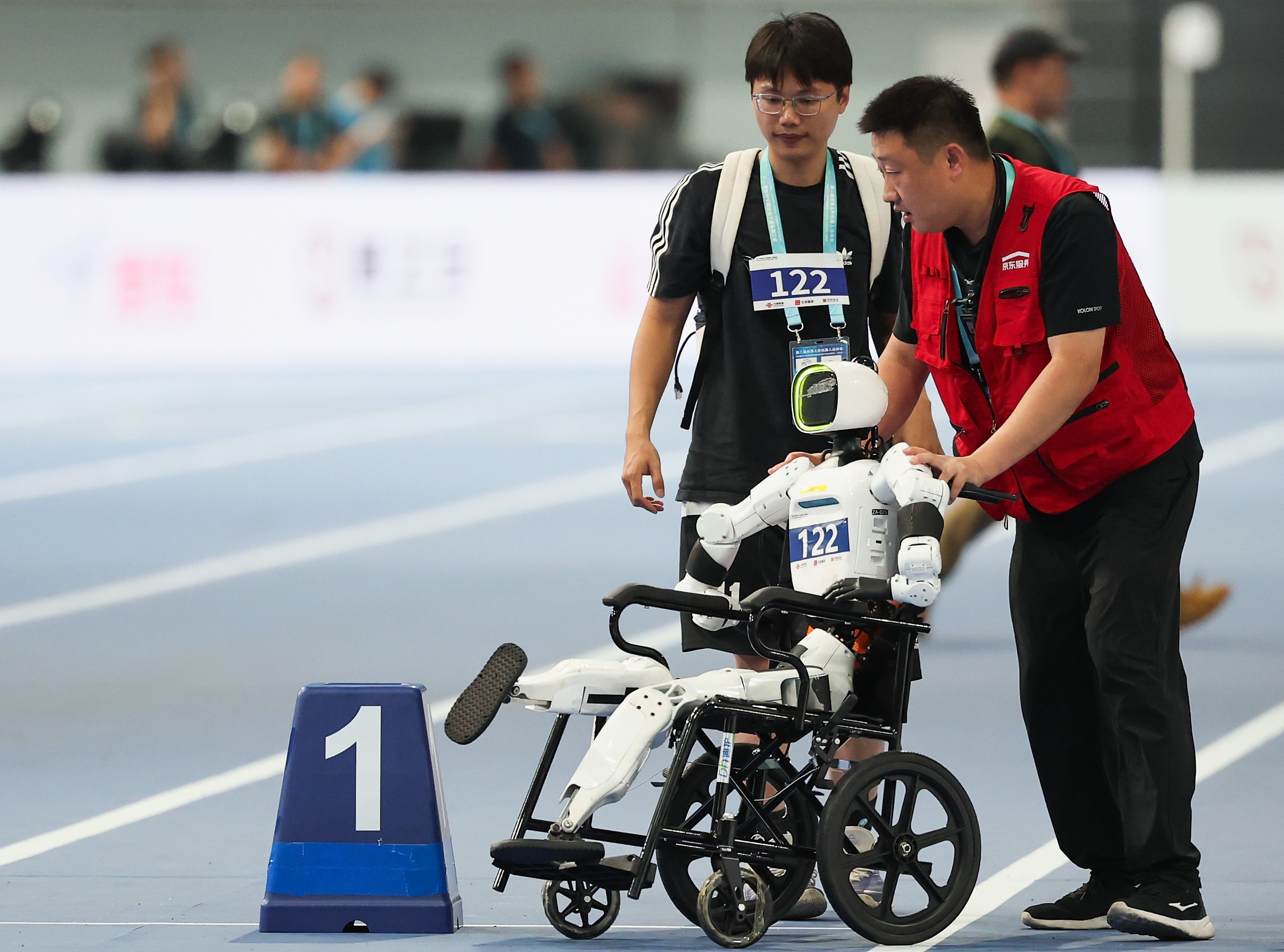 Two staff members remove a malfunctioning robot, seated in a wheelchair.
