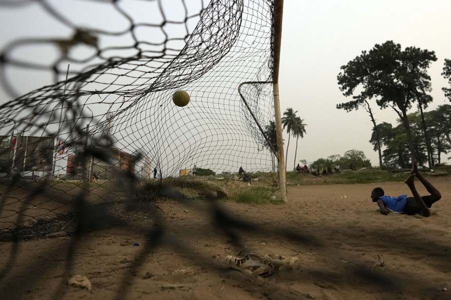 A young man watches the ball after diving while playing soccer on a dusty field.