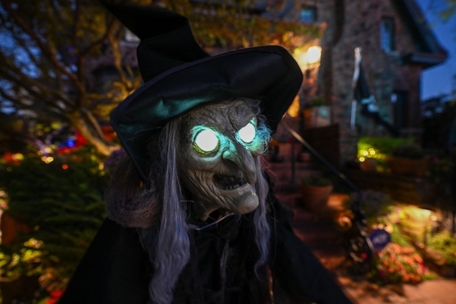 A scary witch decoration with glowing eyes stands outside a house.