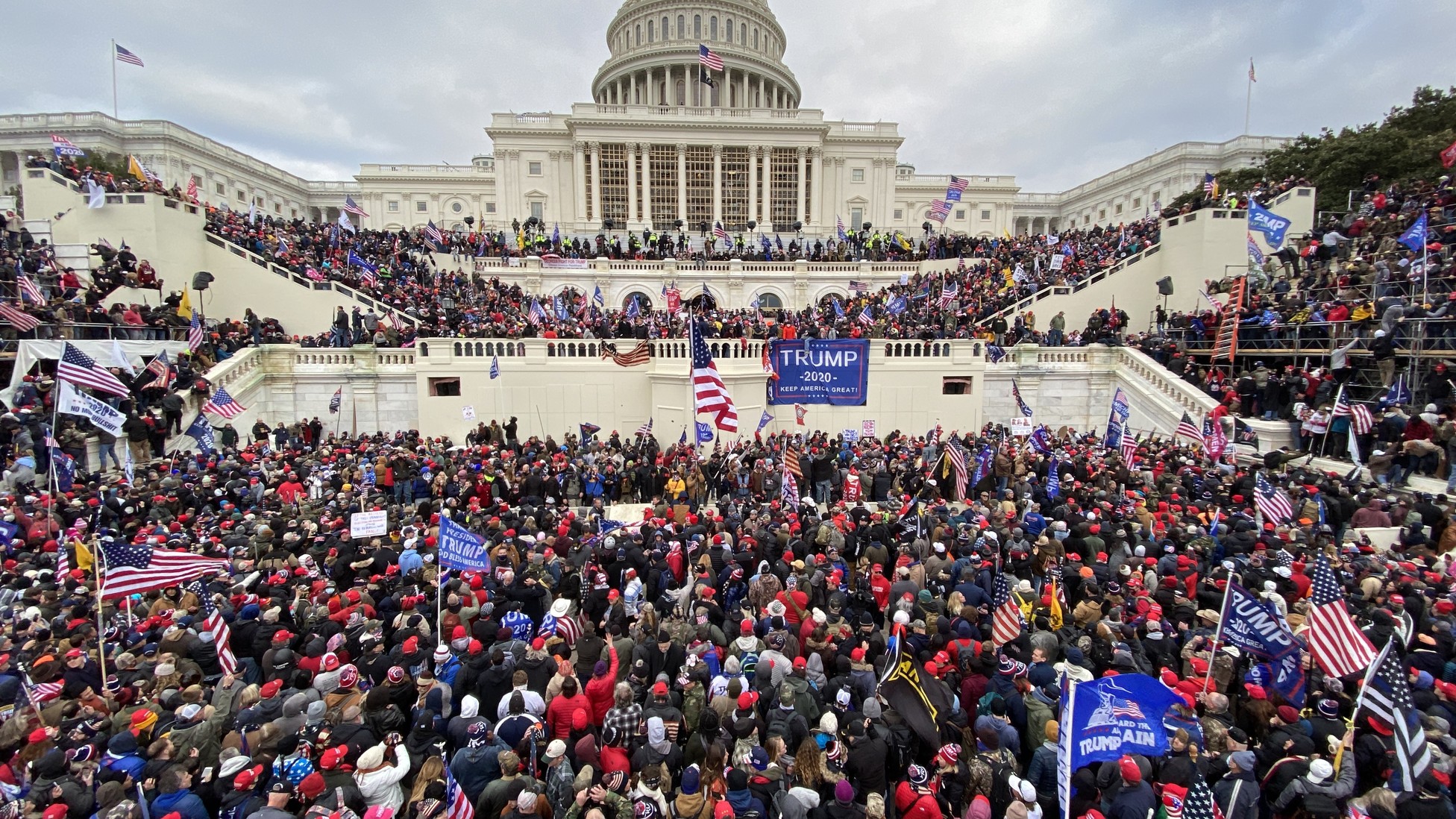 A photograph of hundreds of people gathered outside the U.S Capitol, waving American flags and Trump banners.