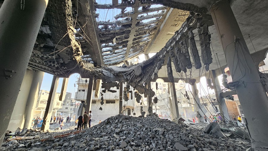 People stand beside piles of rubble under the destroyed roof of a mosque.
