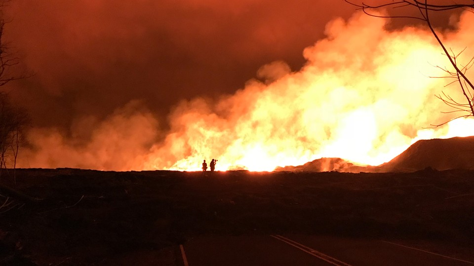 A red sky and yellow-lit smoke background USGS scientists working in front of the actively outgassing Fissure 8 vent, in Hawaii.