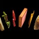 A book floats in the air between two buns, a piece of lettuce, two tomato slices, and American cheese.