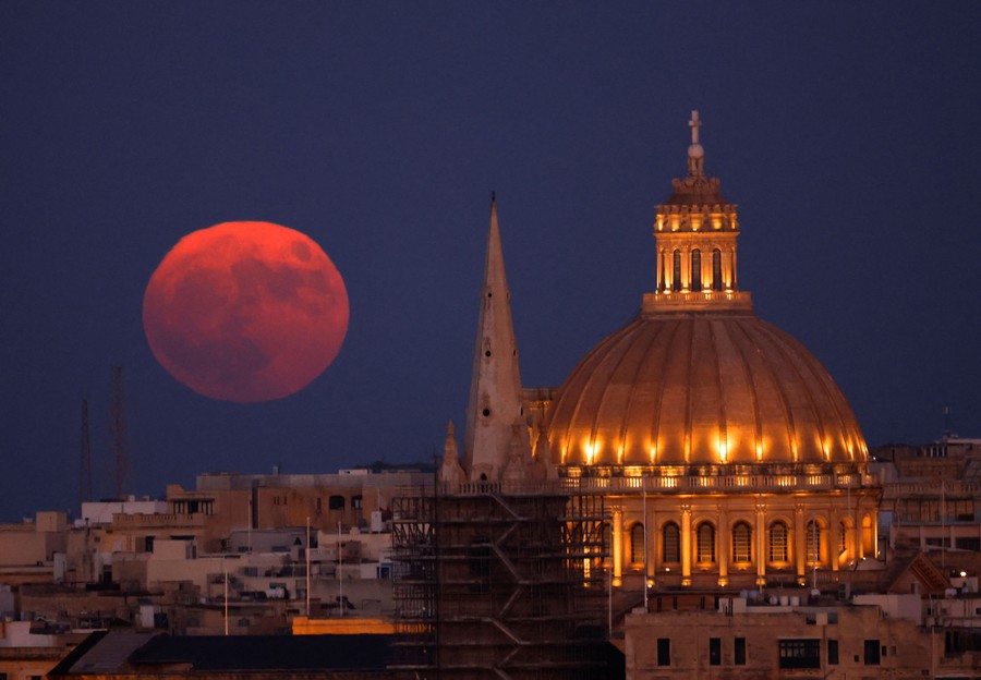 A full moon rises, seen behind a cathedral and a basilica.