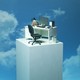 An office desk sits on a pillar high up in the clouds.