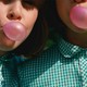 two girls wearing matching green gingham shirts and blowing pink gum bubbles