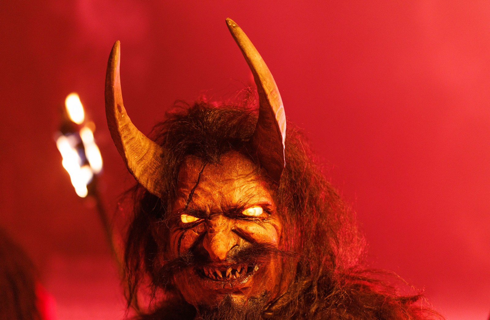 A person performs while wearing a scary Krampus mask with horns.