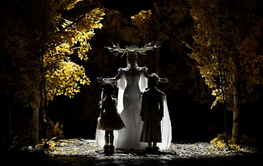 A woman and two children stand silhouetted on a runway during a fashion show.