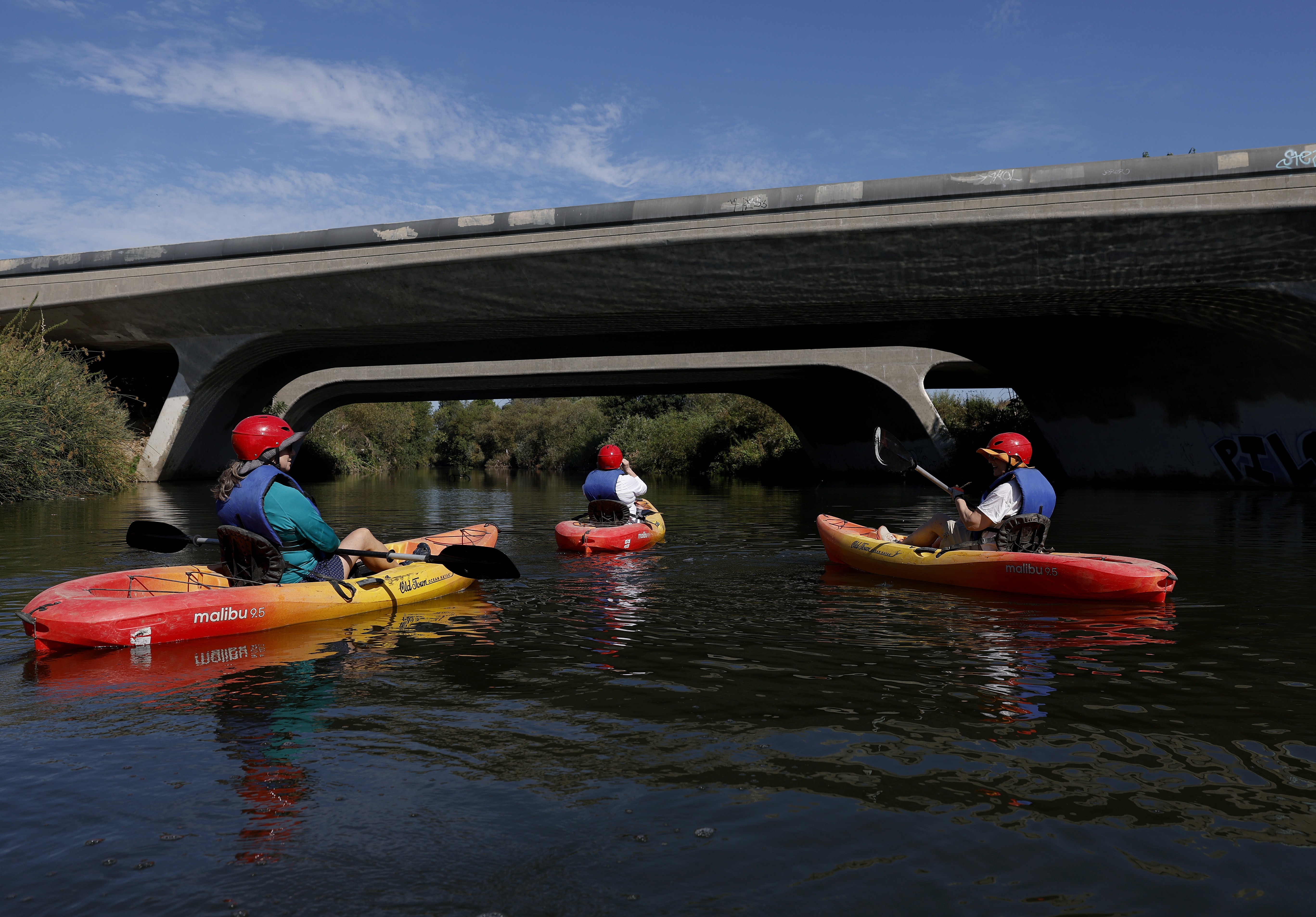 Kayakers paddle along a river beneath a road bridge.