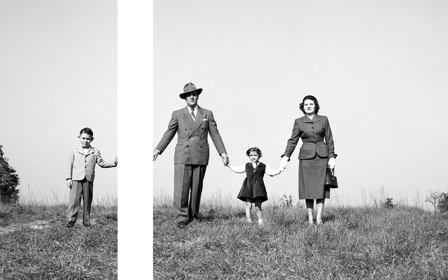 A black and white image of a family holding hands on a hill, with a gap between the son's hand and the father's