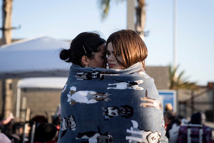 Two women embrace outside, wrapped in a single blanket.
