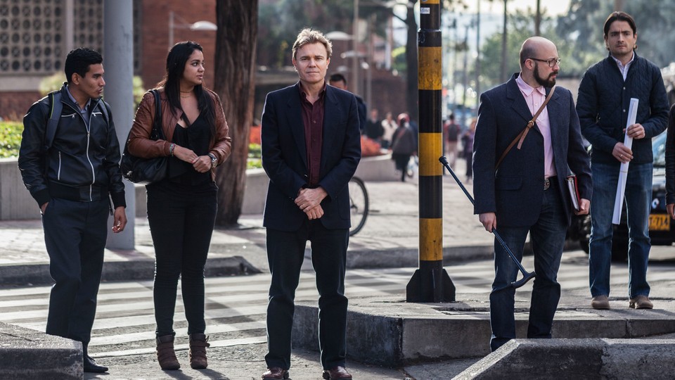 A group of people waits for a pedestrian light at a street corner in Colombia.