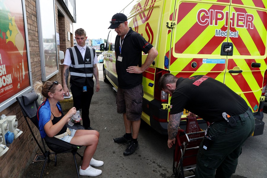 A woman sits with a water bottle as several paramedics tend to her.