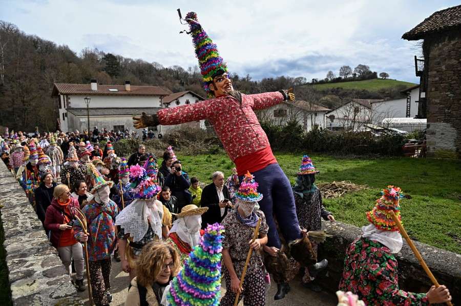 Villagers in traditional costumes march with a large puppet in a small parade.