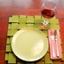 A place setting for one: A light green plate on a green woven placemat with a knife and fork sitting on a plaid napkin. A half-full glass of wine sits by the plate.