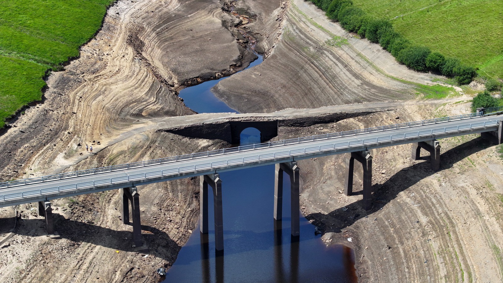 An aerial view of a mostly-dry reservoir, with one new road bridge, and another abandoned, smaller bridge.