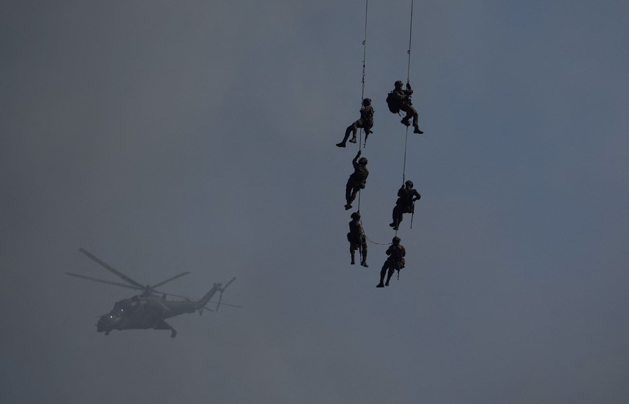 Six soldiers dangle from lines beneath a helicopter (out of frame).