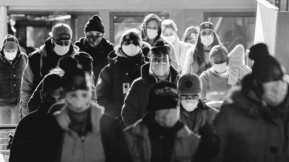 People stand together wearing masks and bundled in warm clothing.