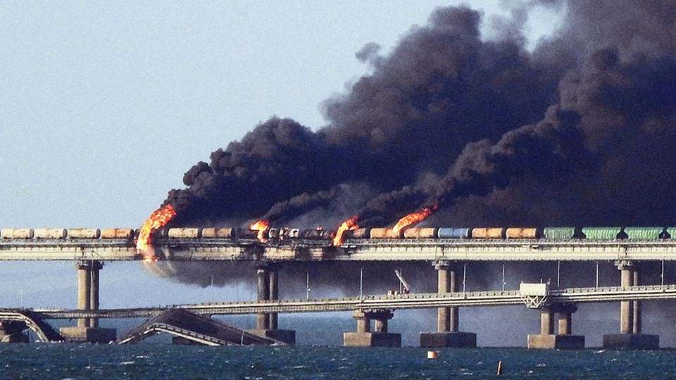 Black smoke billows from a train on a bridge.