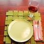 A place setting for one: A light green plate on a green woven placemat with a knife and fork sitting on a plaid napkin. A half-full glass of wine sits by the plate.
