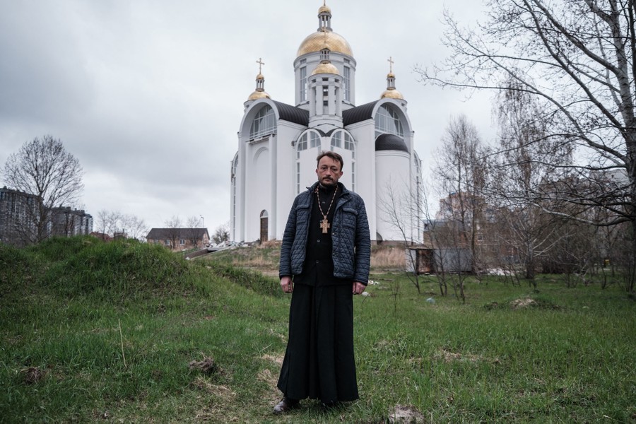A priest stands outside a church building.