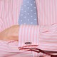 Close-up of a torso of a man wearing a pink dress shirt with cuff links and a blue tie, his arms crossed.