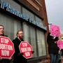 Protsters stand outside a Planned Parenthood clinic holding signs.