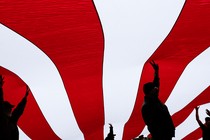 Silhouettes of people hold up a giant flag with red and white stripes