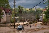 Four people walk through a muddy suburban street intersection, inspecting the flood damage in Asheville, North Carolina, in the aftermath of Hurricane Helene