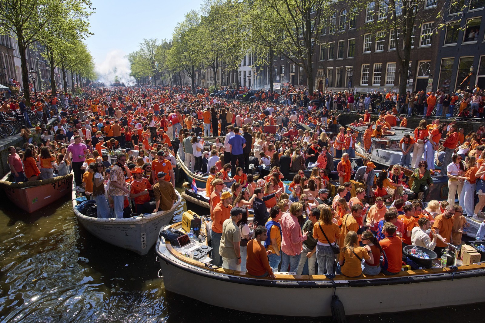 Hundreds of people wearing orange gather in many boats, crowded together in a broad canal.