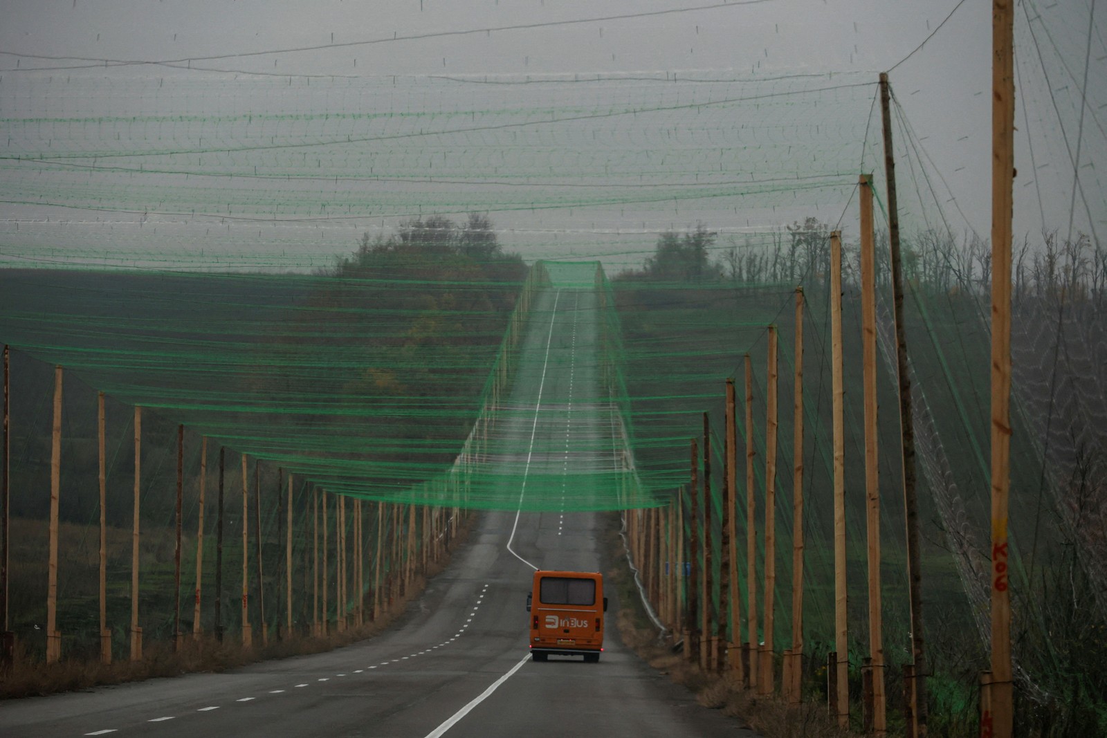 A car drives along a road covered with anti-drone netting, supported by tall poles on either side of the road.