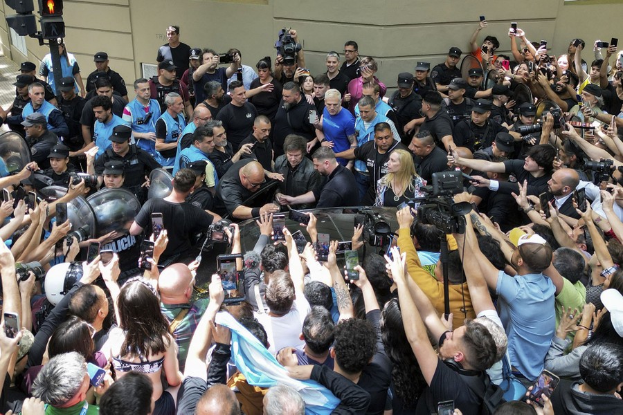A crowd of onlookers and press gathers around a presidential candidate as he enters a car.