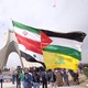 A man carries a giant flag made of flags of Iran, Palestine, Syria and Hezbollah in Tehran.