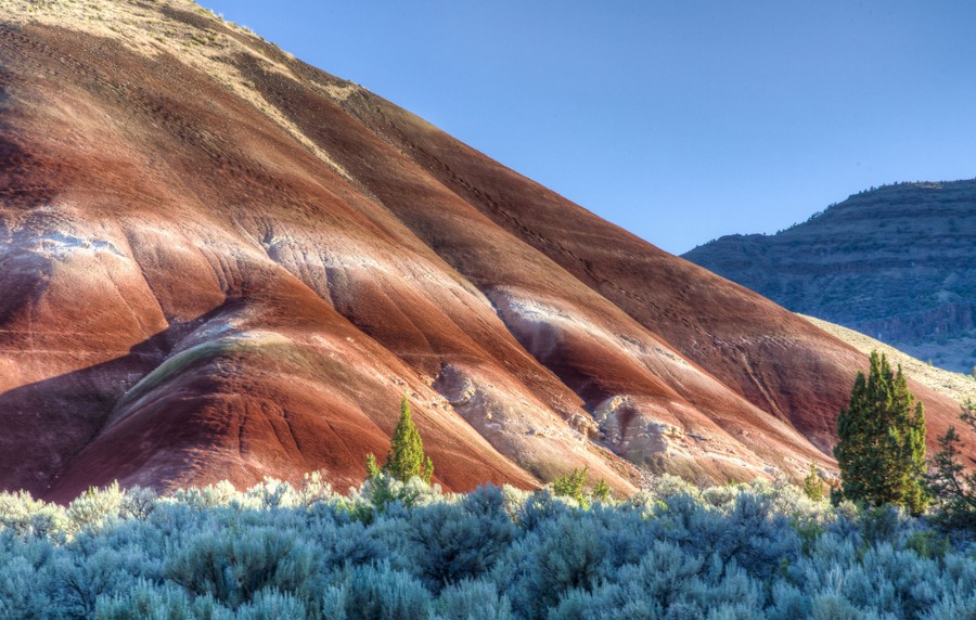 A rounded rock formation, striped white and red, stands above a scrubby valley floor.