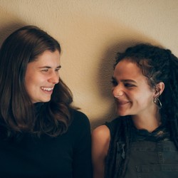 Frances and Bonnie sitting side by side smiling at each other in a scene from 'Conversations With Friends'